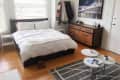 Cozy bedroom with a white bed, wooden dresser, wall art of a bridge, and a small coffee table with magazines.
