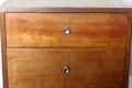 Wooden two-drawer nightstand with round metal knobs on a dark wood floor.
