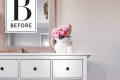 White dresser with black knobs, pink flowers in a vase, and a mirror above on a wooden floor.