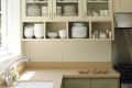 Kitchen with beige cabinets, open shelving displaying white dishes, stainless steel stove, and cookies on the counter.