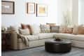 Beige sectional sofa with patterned throw pillows, round leather ottoman, framed art, and a vase with branches in a cozy living room.
