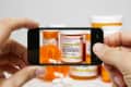 Hands holding a smartphone capturing a photo of orange prescription pill bottles.