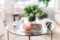 Glass coffee table with pink candle, white tulips in a vase, and decorative bowls in a bright living room.