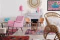 Eclectic living room with pink chair, rattan furniture, colorful rugs, sunburst mirror, and playful wall art.