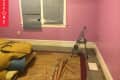 Empty room with pink walls, broken blinds, a small ladder, and scattered wooden planks on the floor.