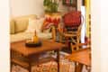 Cozy living room with a ceiling fan, green plant, beige sofa, colorful cushions, wooden coffee table, and bookshelves.