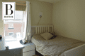 Small bedroom with beige walls, a bed with neutral bedding, white headboard, and a window with blinds and curtains.