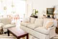 Living room with beige sofa and armchair, wooden coffee table, dining area with round table and chairs, and decorative plants.