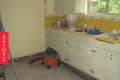 Old kitchen with yellow countertops, cluttered sink, cleaning supplies, and a vacuum cleaner on the floor.