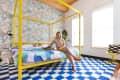 Bright bedroom with yellow canopy bed, colorful bedding, geometric wallpaper, and a woman petting a cat on the bed.