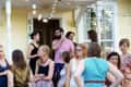 Group of people socializing on a porch with string lights and a yellow house in the background.