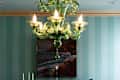 Dining room with green chandelier, striped walls, set table, and landscape painting above a sideboard.