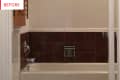 Bathtub with brown tile wall, chrome faucet, and wooden cabinet.