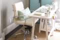Home office with white desk, swivel chair, gallery wall, and blue louvered doors.