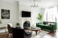 Living room with green velvet sofa, black armchairs, white fireplace, large window, and modern chandelier.
