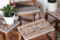 Wooden stools with floral stenciled tops, each holding a potted plant, including snake plant and rubber plant.