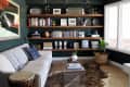 Living room with a white sofa, wooden shelves filled with books and decor, a glass coffee table, and a large window.