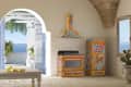 Colorful kitchen with ornate fridge and stove, arched doorway to sea view, lemons on table, and cactus by window.