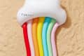 Cloud-shaped pool float with rainbow stripes on sandy surface.