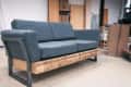 Gray sofa with metal frame and wooden base in a workshop setting, surrounded by tools and boxes.