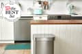 Modern kitchen with stainless steel trash can, wooden countertop, mint green appliances, and white cabinets.