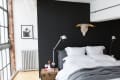 Modern bedroom with black accent wall, white bedding, gray throw, bull skull decor, and industrial lamps.