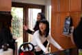 Three women smiling and talking in a kitchen with wooden cabinets and a glass door.