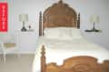 Traditional bedroom with ornate wooden bed, white bedding, wicker chair, and two side tables with lamps.