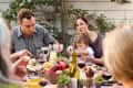 Family gathering around an outdoor table with wine, bread, and a centerpiece of fruits and succulents.