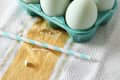 Six pale blue eggs in a teal ceramic egg holder on a striped towel.