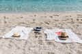 Two beach towels on sand with straw hats, flip-flops, and clear blue water in the background.
