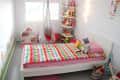 Child's bedroom with a colorful striped bedspread, hanging chair, toy shelf, and wall decorations.