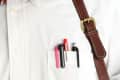 White shirt with ink-stained pocket holding pens, paired with a striped bow tie and brown leather strap.
