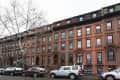 Row of brownstone townhouses with parked cars and bare trees on a city street.