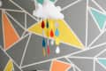 White crib in a nursery with geometric wall design and cloud mobile with colorful raindrops.