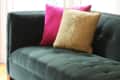 Green velvet sofa with pink and gold cushions on a colorful striped rug.