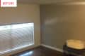 Empty room with beige walls, wooden floor, window blinds, and a baby seat on a metal crate.