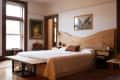 Bedroom with a large wooden headboard, white bedding, a bench at the foot, and a chandelier. Artwork and a portrait on walls.