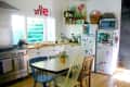 Bright kitchen with wooden floors, colorful chairs, decorated fridge, and a small dining table with flowers.