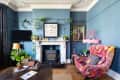 Eclectic living room with blue walls, floral armchair, fireplace, plants, and framed art.