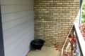 Empty balcony corner with brick and siding walls, black planter, and red foliage.
