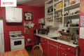 Red kitchen with white cabinets, open shelving, stove, and dish rack by the sink.