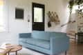 Living room with a blue sofa, black door, wall hooks with bags, and a staircase with plants.