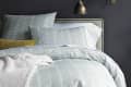 Bed with leaf-patterned bedding, yellow accent pillow, and brass wall lamp on dark wall.