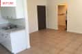 Empty kitchen with white cabinets, stainless steel sink, and beige tiled floor. Person partially visible in doorway.