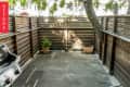 Small patio with wooden fence, potted plants, and a grill on the left. Tree with string lights in the corner.