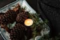 Pinecones and greenery arranged on a decorative plate with a lit candle.