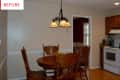 Dining room with wooden table and chairs, chandelier, and view into kitchen with stove and cabinets.