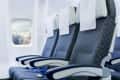 Three airplane seats with blue upholstery and white headrest covers, next to a window showing clouds.