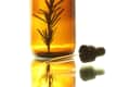 Amber glass bottle with rosemary sprig inside, next to a dropper on a reflective surface.